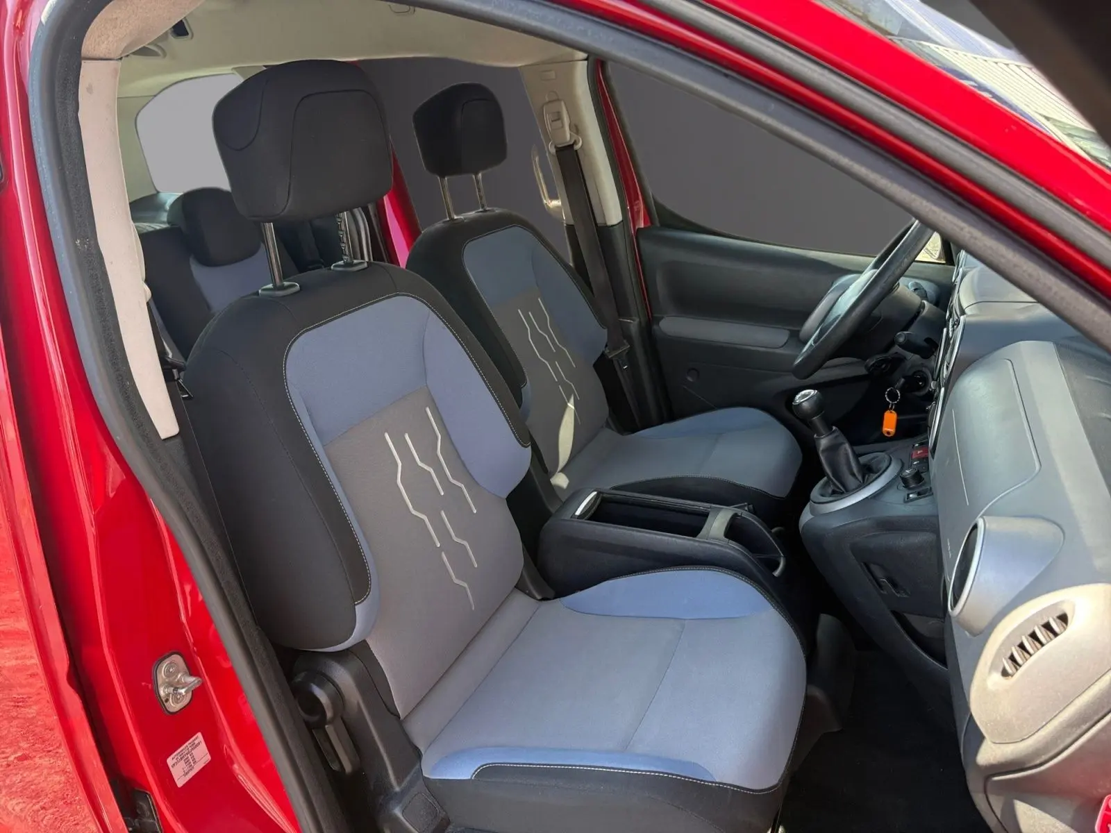 Vue intérieure côté gauche du Peugeot Partner Tepee rouge 2016, montrant sièges avant bi-ton et volant réglable.