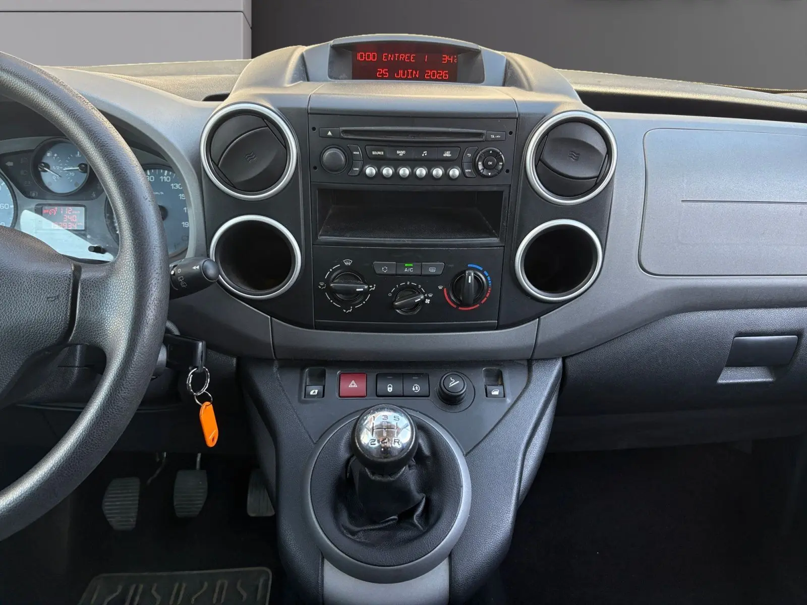 Vue intérieure centrée sur la console centrale et levier de vitesses manuelle du Peugeot Partner Tepee rouge de 2016.