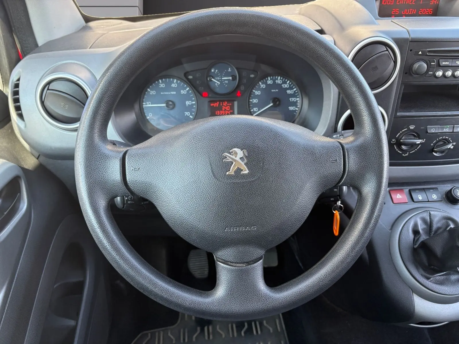 Vue intérieure centrée sur le volant Peugeot noir, tableau de bord et levier de vitesses d’un Partner Tepee rouge de 2016.