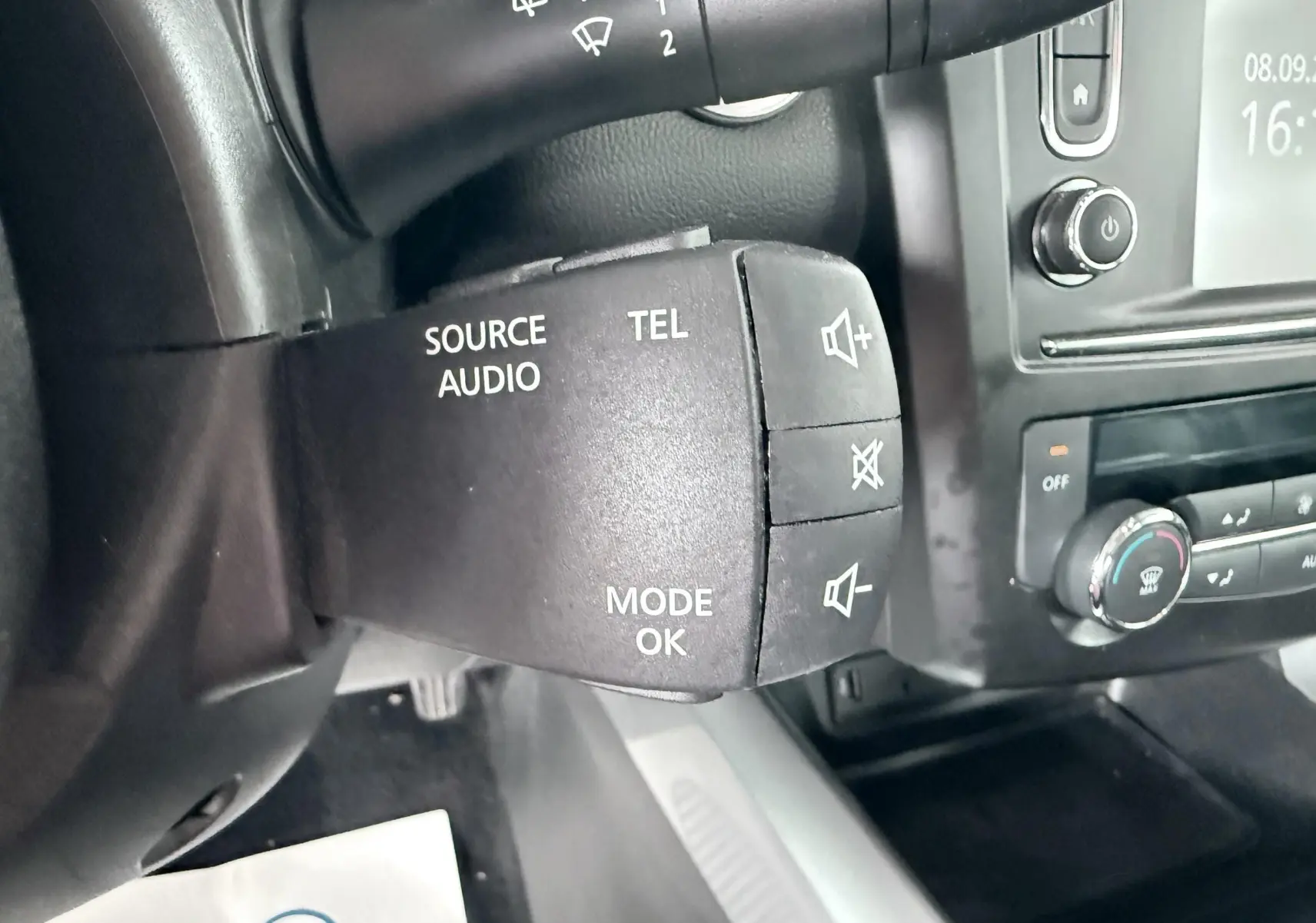 Gros plan sur la commande audio au volant noir dans l'habitacle du Renault Kadjar gris, avec tableau de bord et commandes clim visibles.