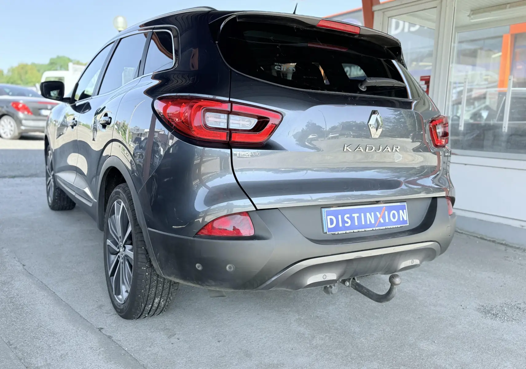 Vue 3/4 arrière droite d’un Renault Kadjar gris avec attelage de remorque et feux arrière allumés.