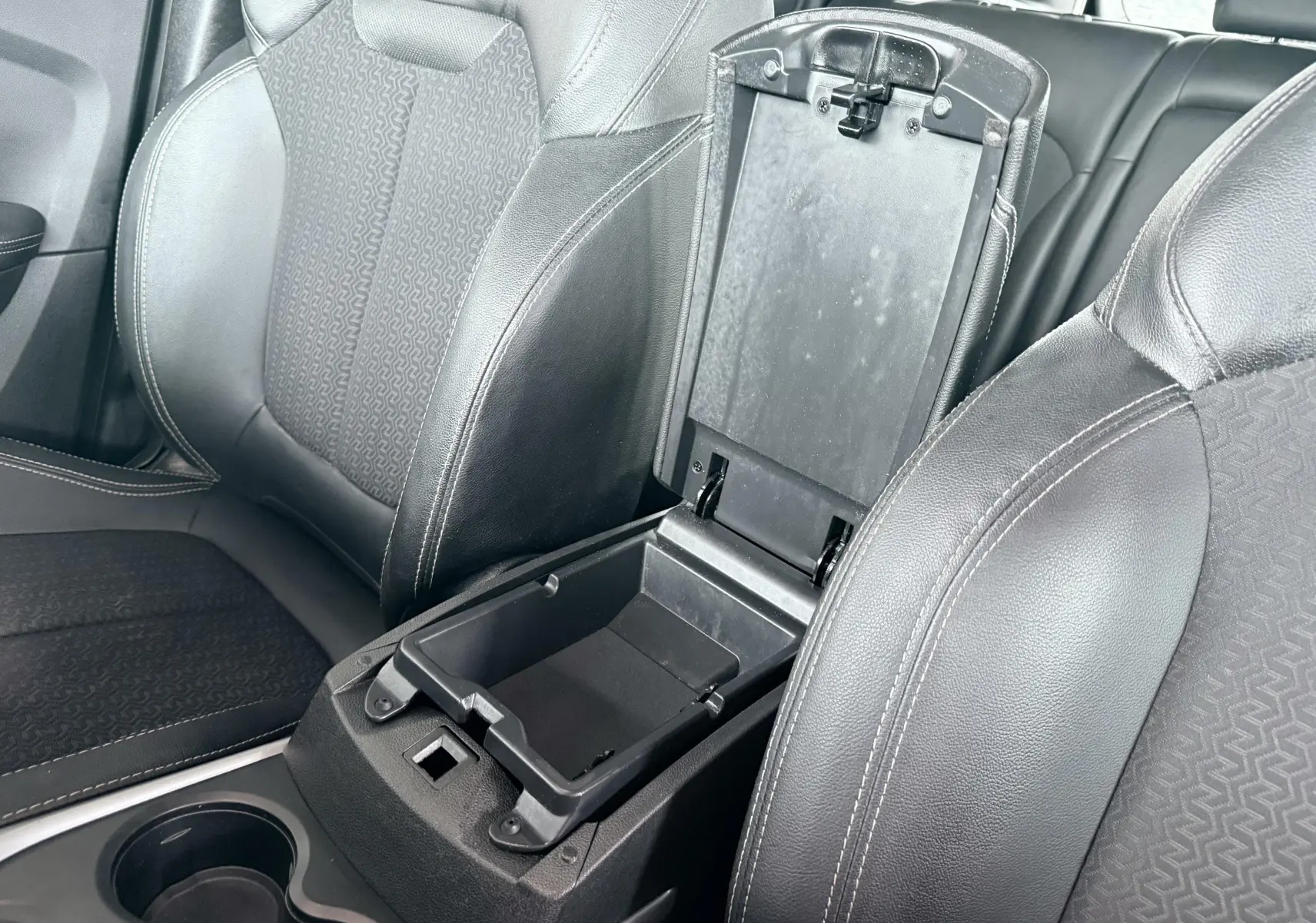 Vue rapprochée de l’intérieur du Renault Kadjar gris, montrant l’accoudoir central ouvert entre les sièges avant en tissu et cuir noir.