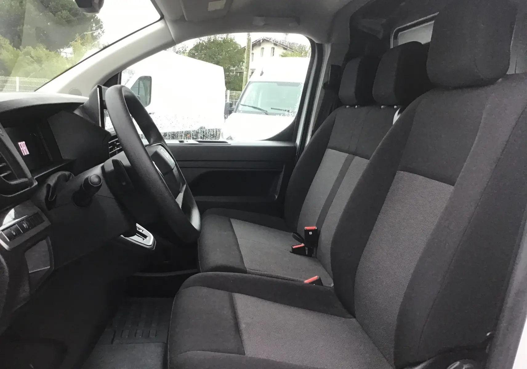Vue intérieure côté conducteur du Fiat Scudo Fourgon blanc 2024, sièges tissu gris et tableau de bord simple.
