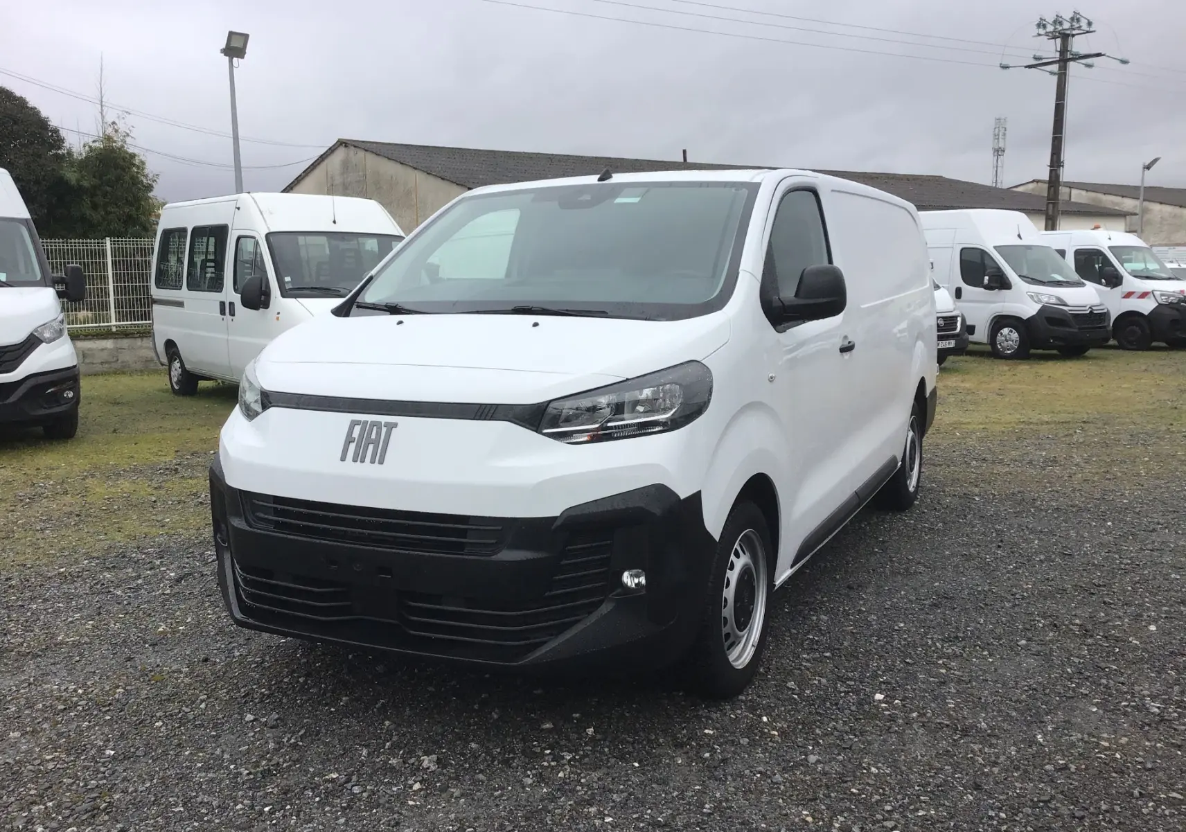 Fourgon FIAT Scudo blanc vu en 3/4 avant droit, avec pare-chocs noir et calandre moderne, stationné sur un terrain extérieur.