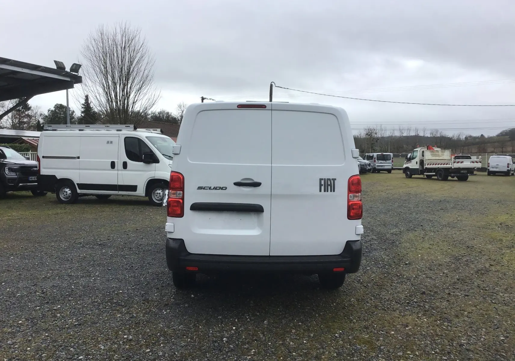 Vue arrière d’un FIAT Scudo Fourgon blanc 2024, avec portes battantes et pare-chocs noir, stationné sur un terrain.