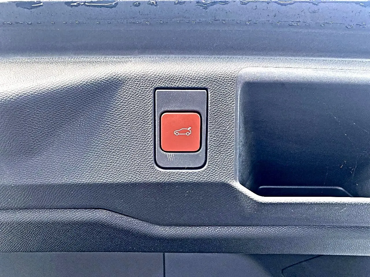 Gros plan sur le bouton rouge d'ouverture électrique du coffre dans l'habitacle noir du Peugeot 5008 Hybrid 145 GT.