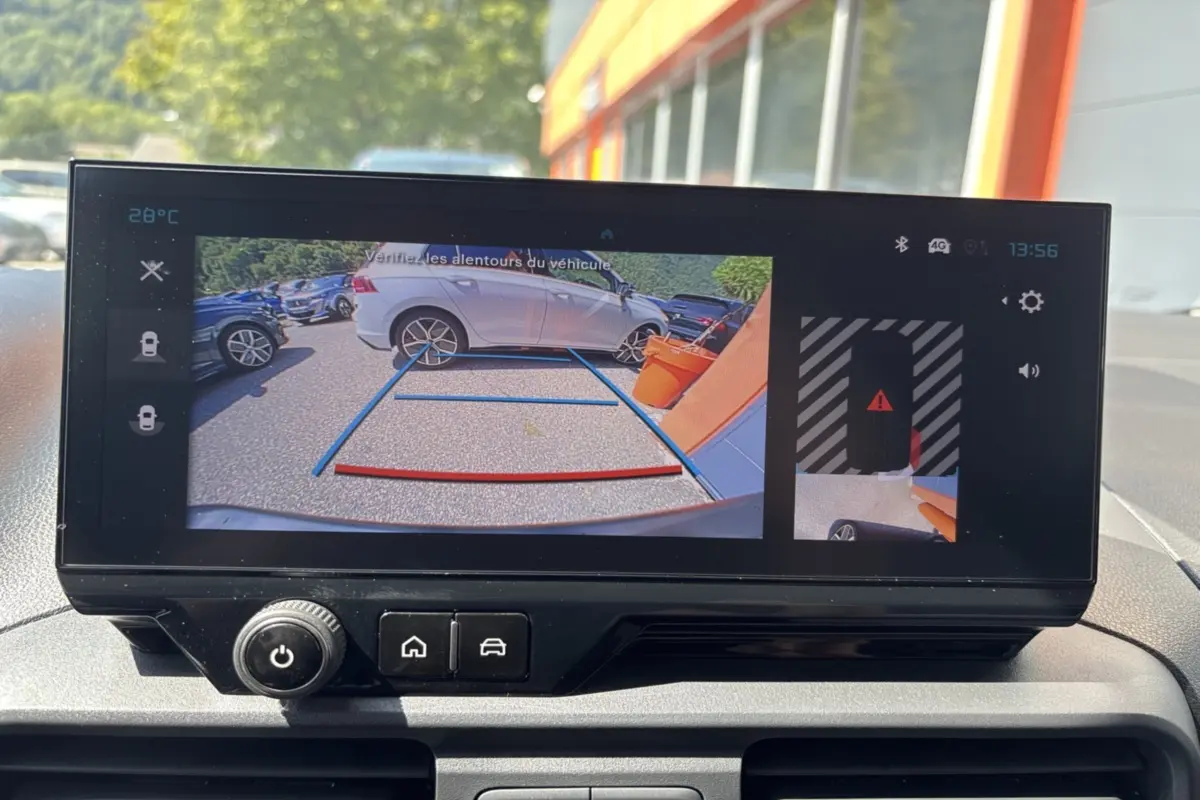 Écran de caméra de recul montrant une voiture grise en 3/4 arrière droite près d’un mur orange.