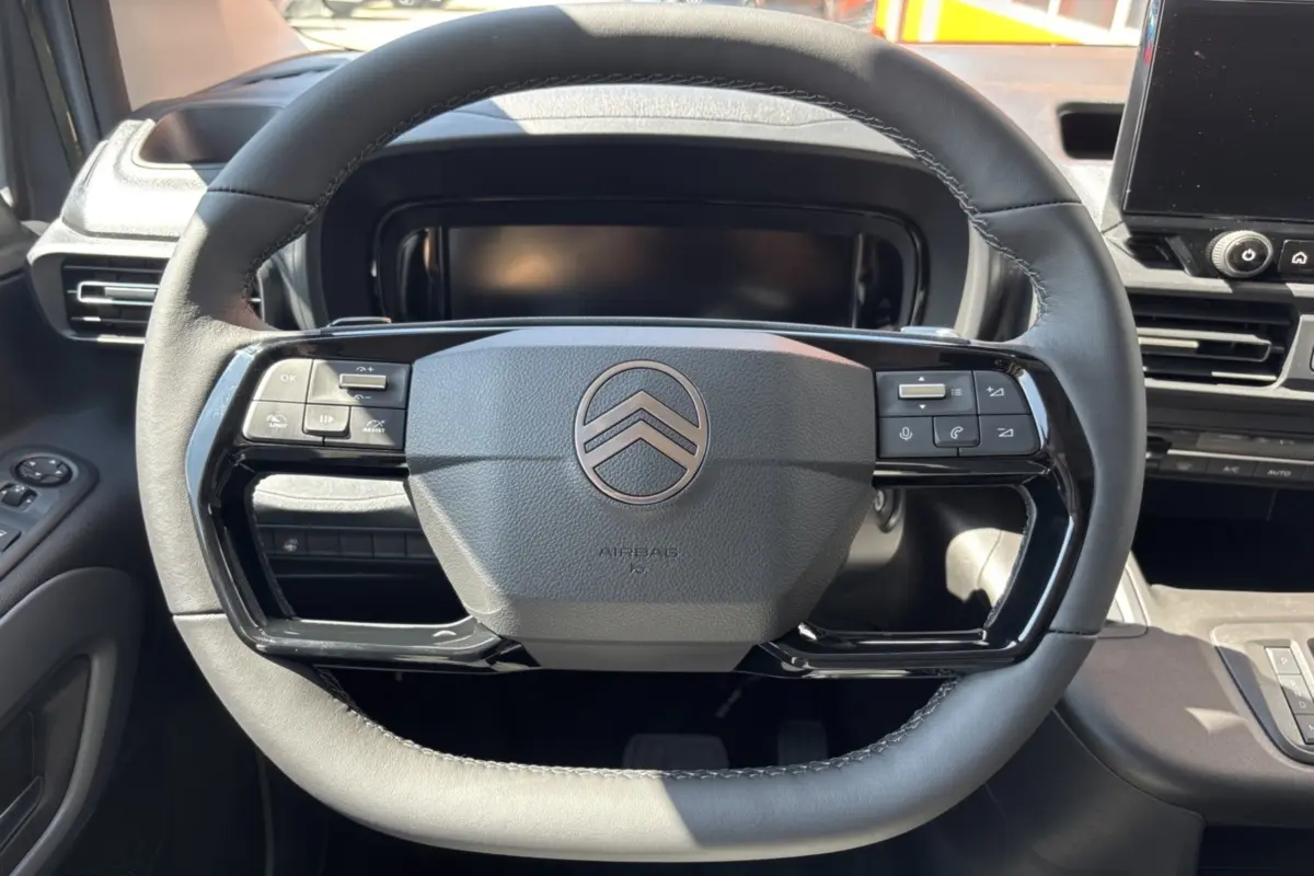 Gros plan sur le volant cuir multifonctions noir du Citroën Berlingo 2026, avec tableau de bord et écran tactile en arrière-plan.