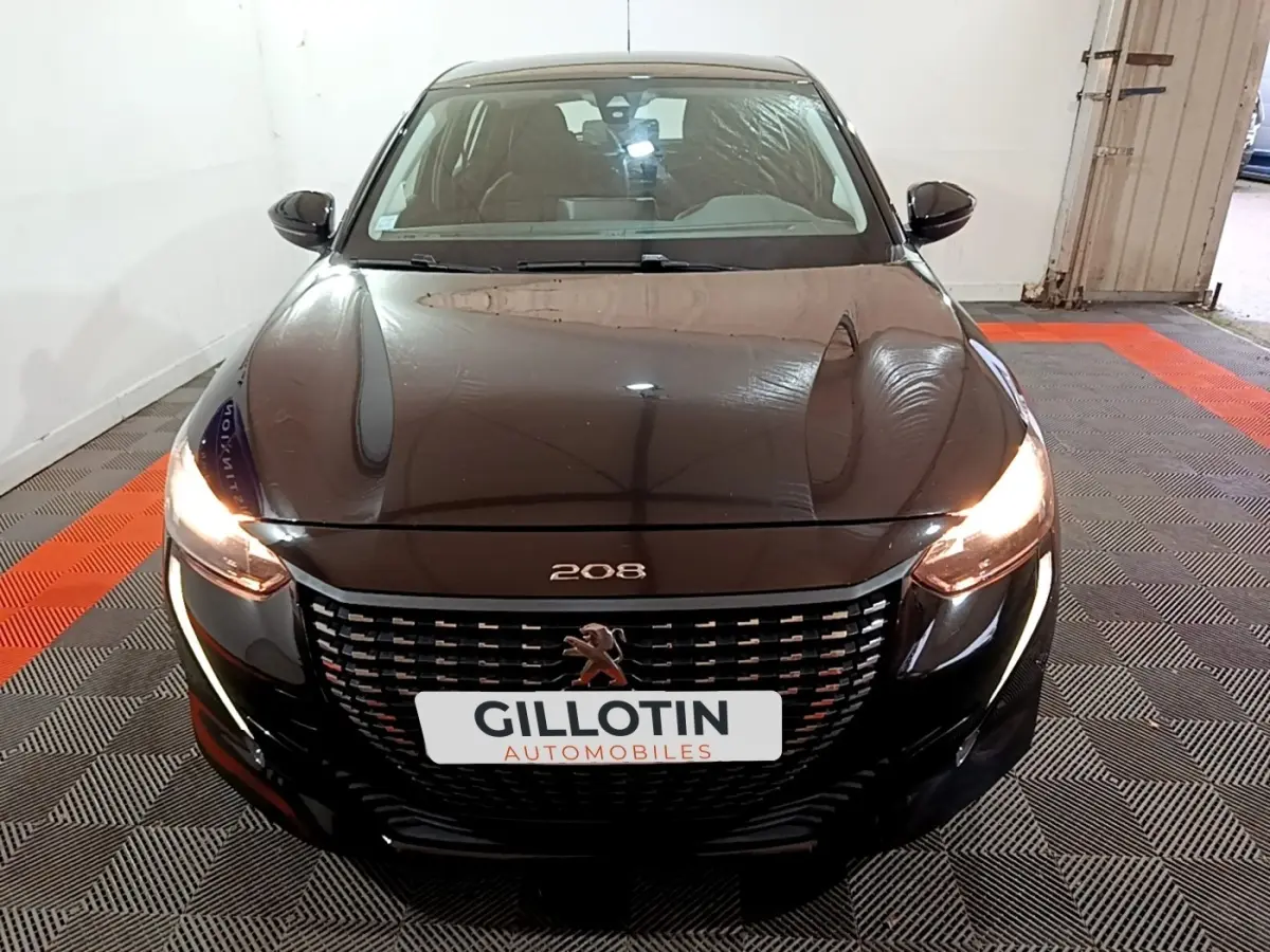 Vue avant d'une Peugeot 208 noire de 2020 avec phares allumés et calandre au lion distinctif.