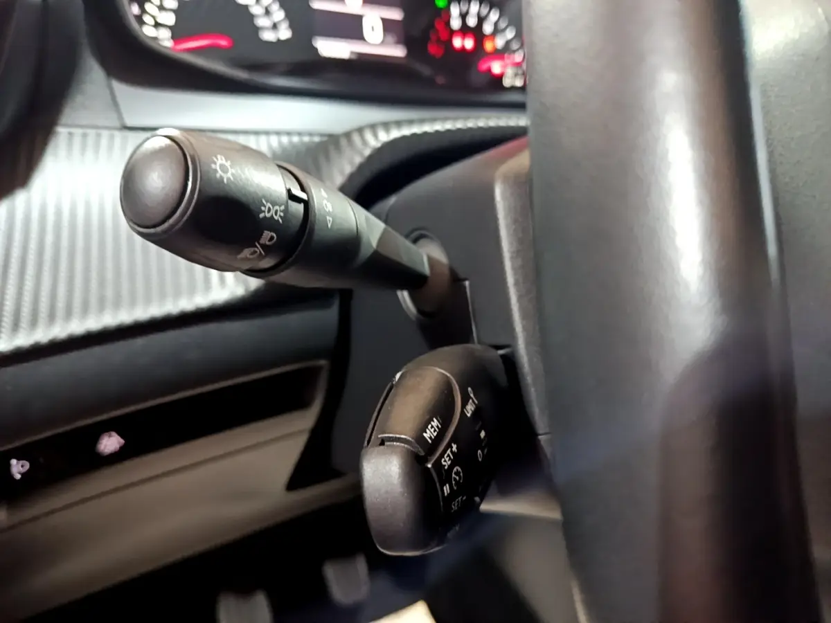 Gros plan sur les commandes au volant noir d’un Peugeot 208 2020, avec tableau de bord numérique en arrière-plan flou.