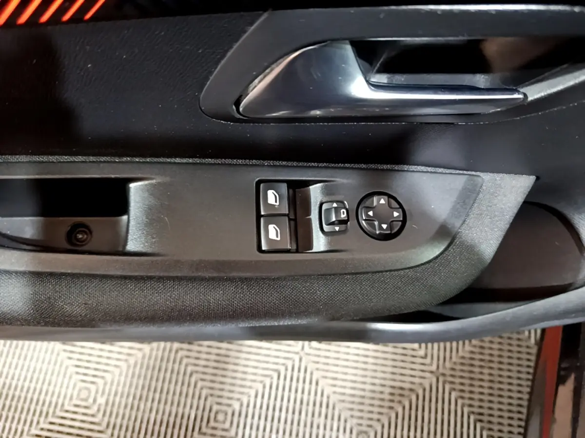 Gros plan sur la commande des vitres et rétroviseurs côté conducteur d'une Peugeot 208 noire, intérieur noir.