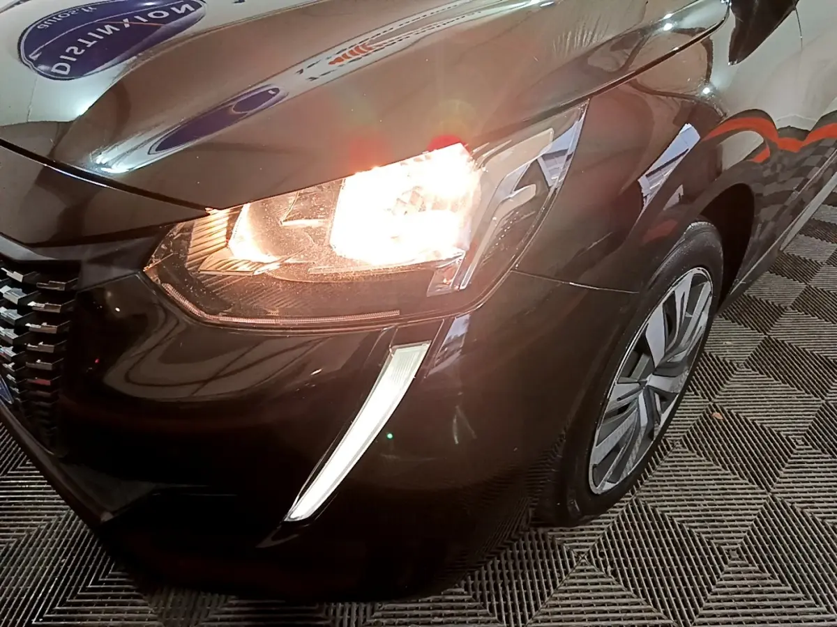 Gros plan sur l'avant droit noir d'une Peugeot 208 2020 avec phare allumé et feux diurnes en forme de griffes.