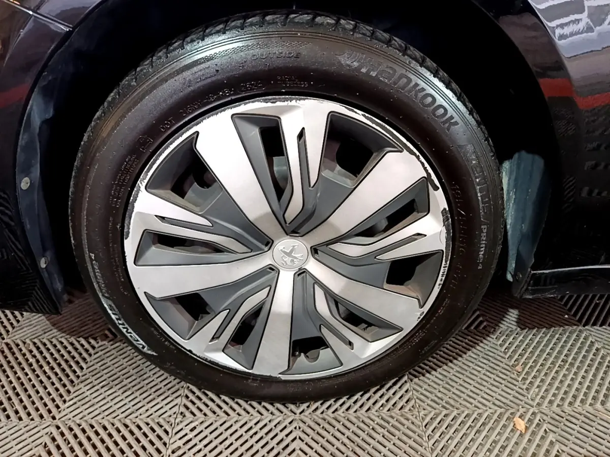 Gros plan sur la roue avant droite d’une Peugeot 208 noire, mettant en valeur la jante aluminium au design moderne.