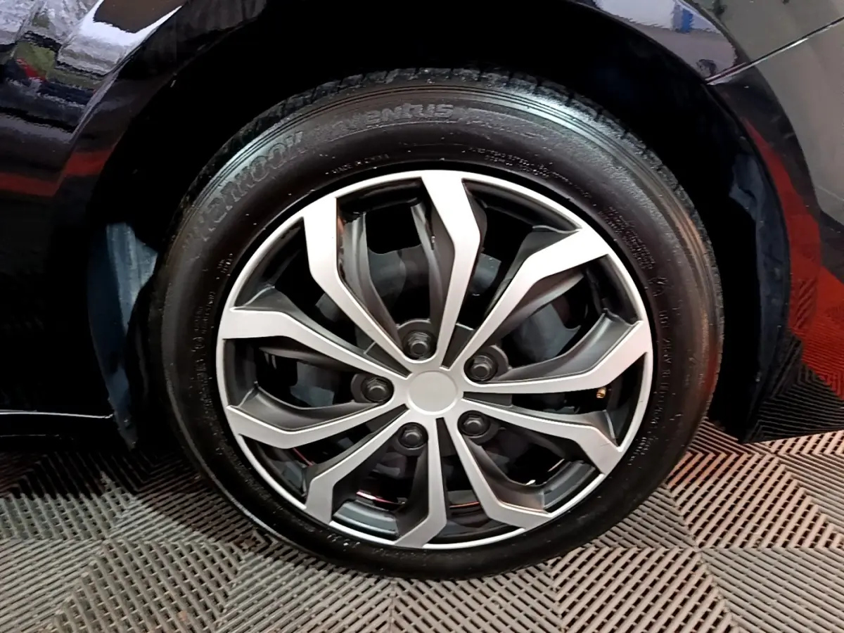 Gros plan sur la roue avant droite d'une Peugeot 208 noire, mettant en valeur la jante alliage au design moderne.