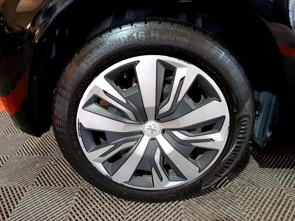 Gros plan sur la roue avant gauche d’une Peugeot 208 noire, avec jante alliage au design moderne bicolore.
