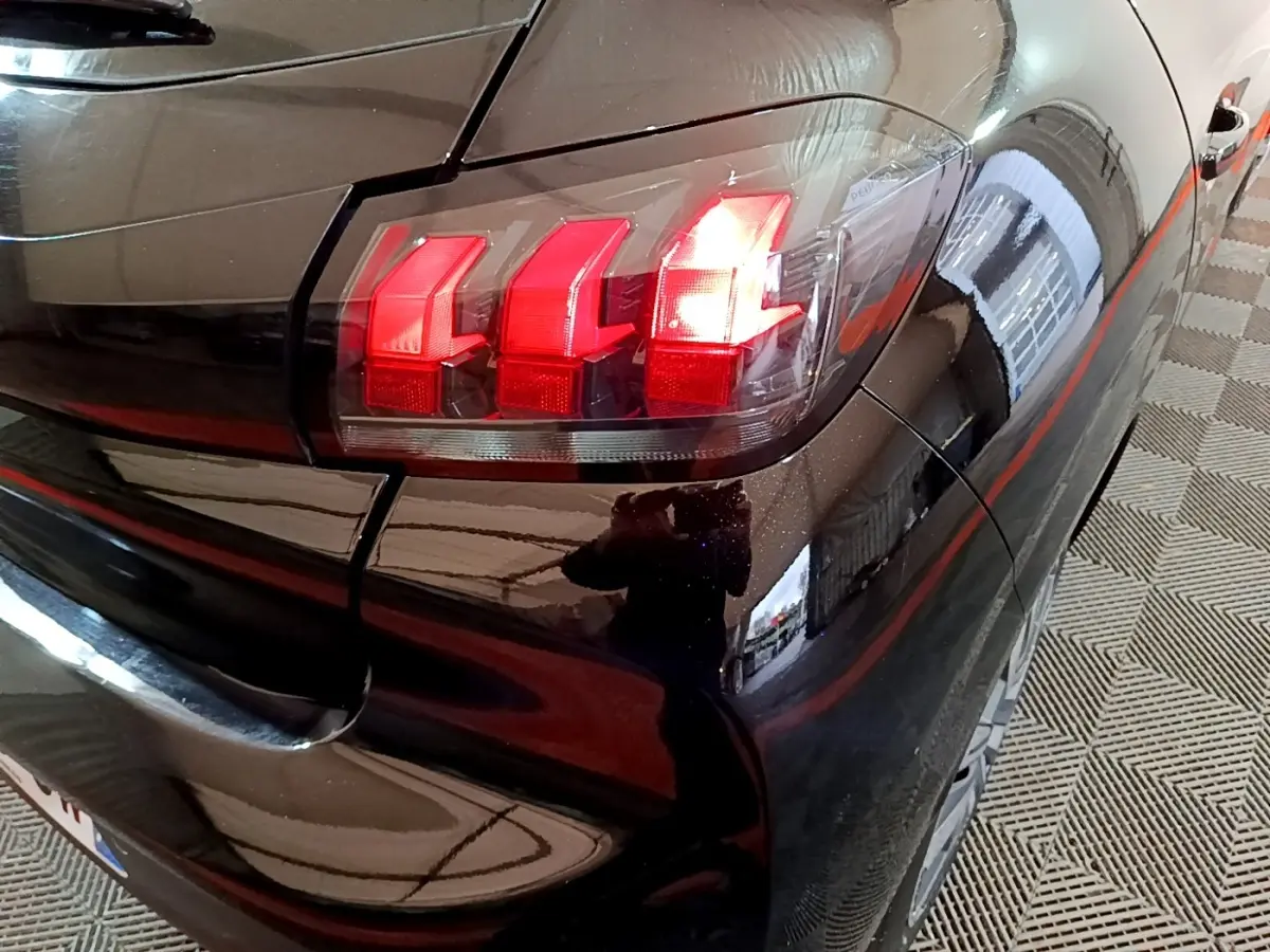 Gros plan sur le feu arrière droit rouge d'une Peugeot 208 noire, vue depuis l'arrière côté droit.