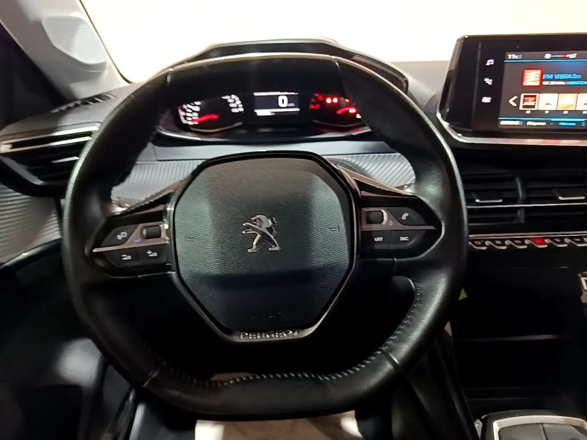 Vue intérieure centrée sur le volant cuir noir de la Peugeot 208 2020 avec tableau de bord numérique et écran tactile.