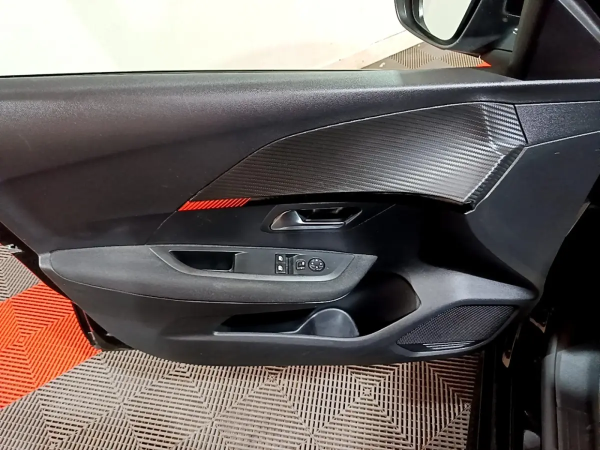 Gros plan sur la porte intérieure côté conducteur de la Peugeot 208 noire, avec commandes électriques et finition effet carbone.