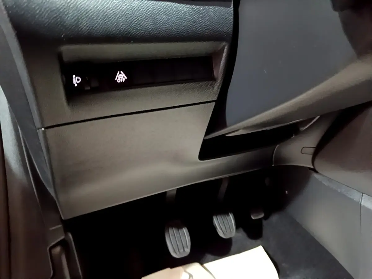 Vue rapprochée du côté gauche sous le tableau de bord noir de la Peugeot 208 avec pédales manuelles et commandes éclairées.