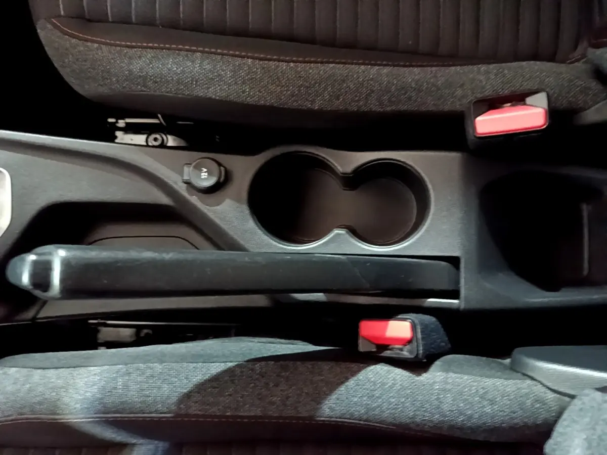 Vue plongeante sur la console centrale noire de la Peugeot 208 avec frein à main manuel et deux porte-gobelets.