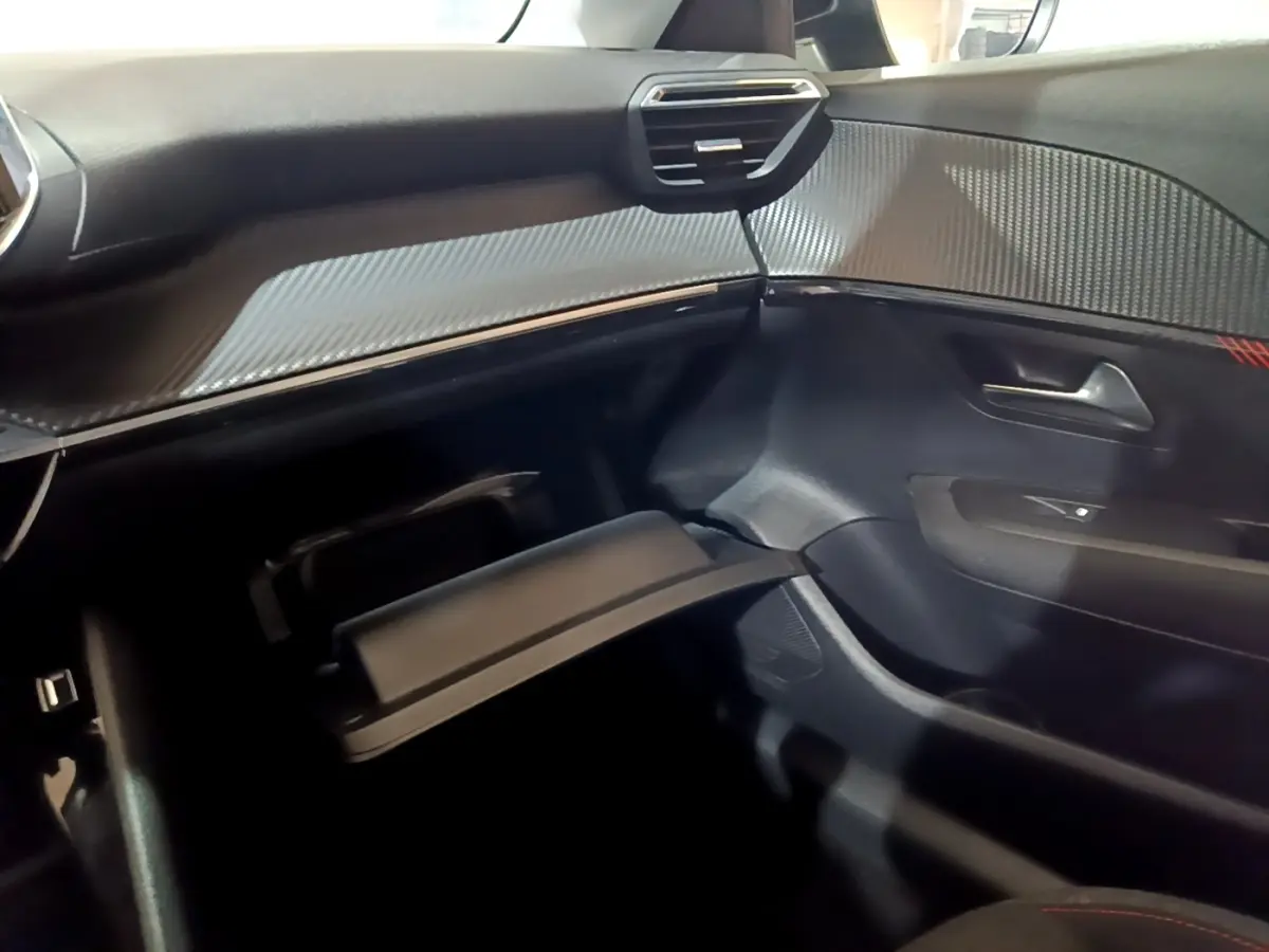 Vue intérieure côté passager de la Peugeot 208 noire, avec boîte à gants ouverte et tableau de bord texturé gris.