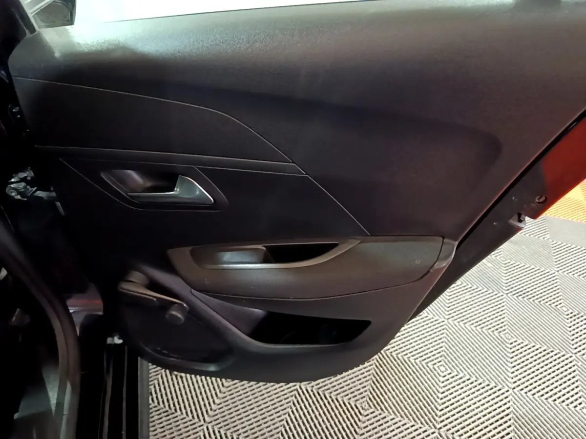 Vue rapprochée de la porte arrière gauche noire d’une Peugeot 208 avec poignée intérieure argentée et rangement intégré.
