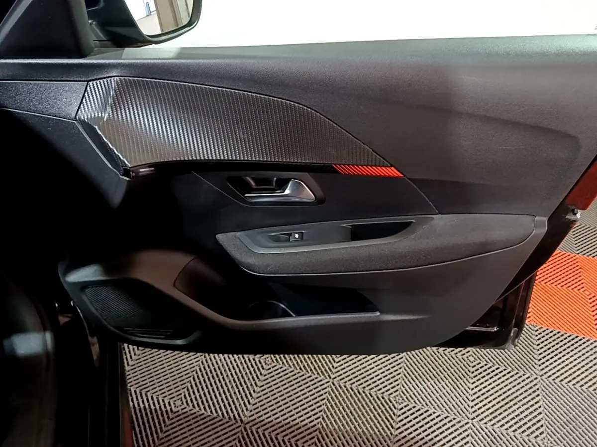 Vue intérieure côté gauche de la porte avant noire de la Peugeot 208 avec insert décoratif carbone et bande rouge.