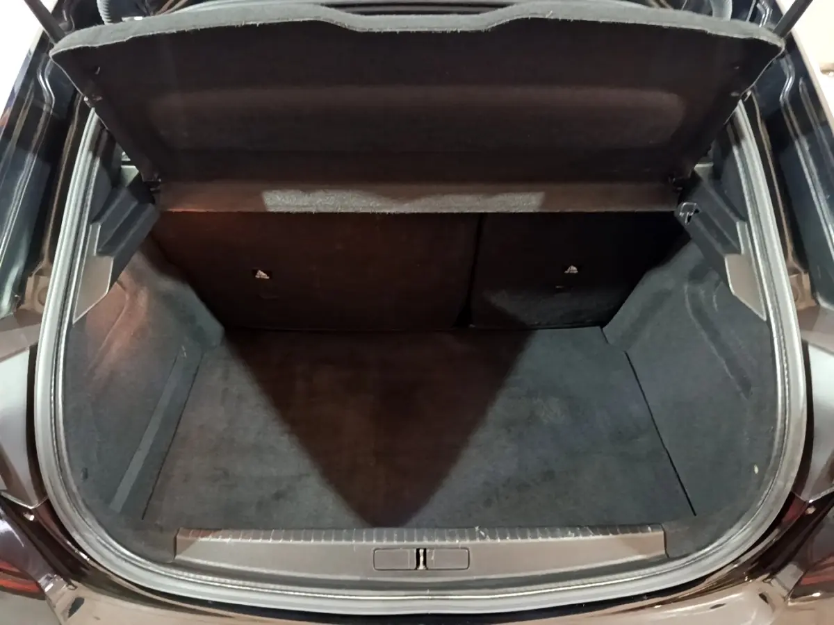 Coffre ouvert vu de l'arrière d'une Peugeot 208 noire, intérieur spacieux et revêtement sombre.