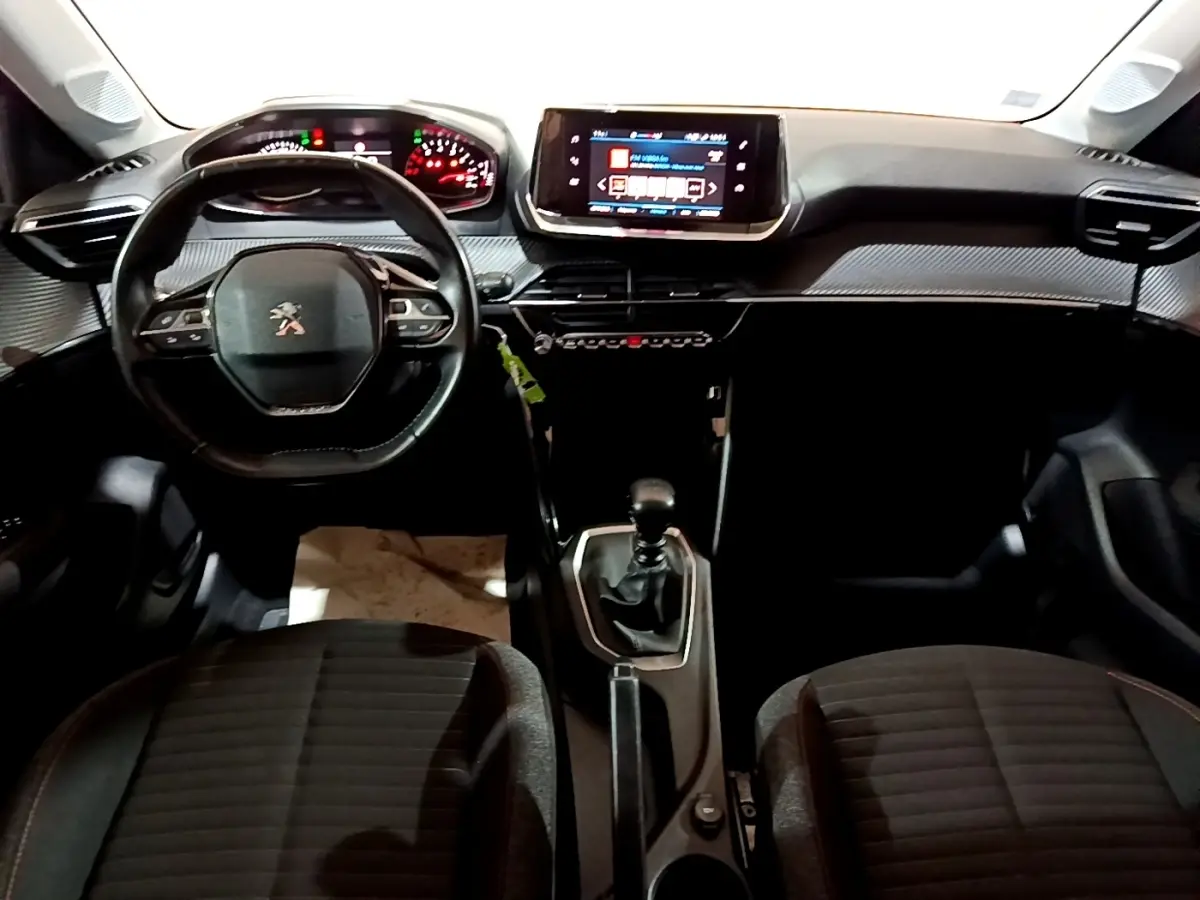 Vue intérieure frontale du tableau de bord noir de la Peugeot 208 avec volant cuir, écran tactile central et boîte manuelle.