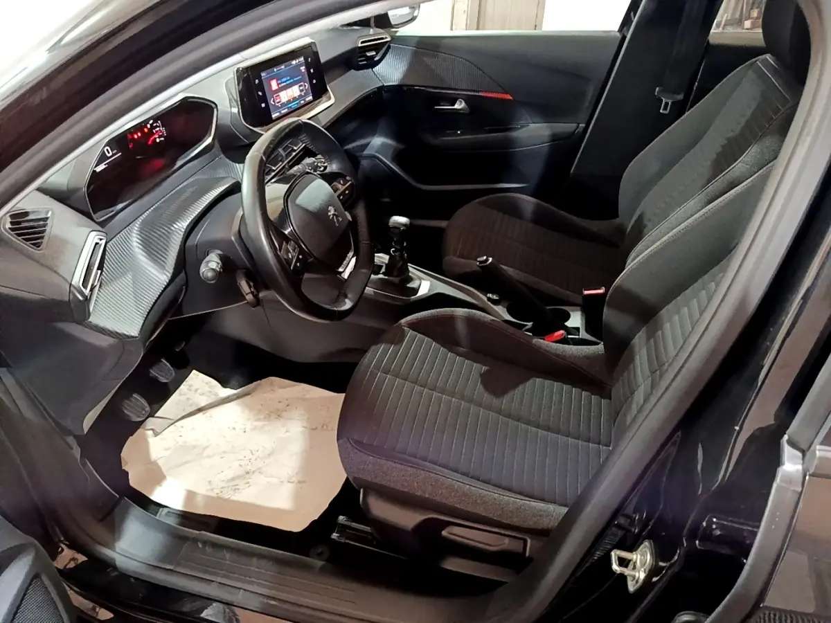 Vue intérieure côté conducteur de la Peugeot 208 noire, montrant le tableau de bord avec écran tactile et volant cuir multifonctions.