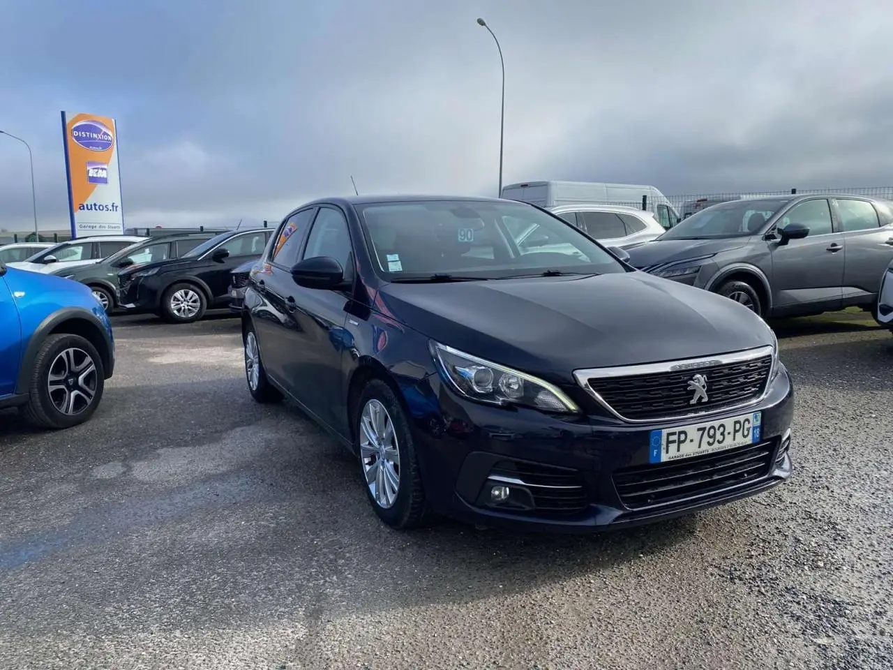 Peugeot 308 bleu foncé vue 3/4 avant droit sur parking avec calandre chromée et phares LED.