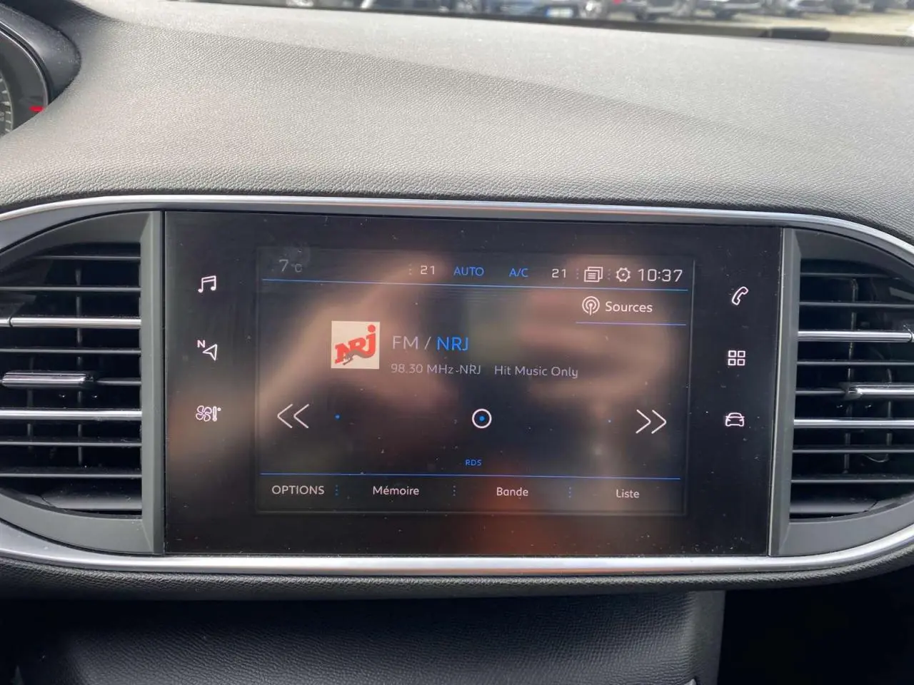 Écran tactile central de la Peugeot 308 2018 affichant la radio FM NRJ, entouré de grilles d'aération noires.