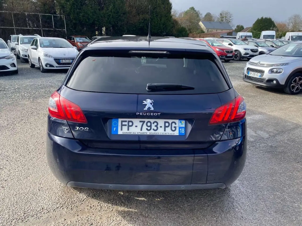Vue arrière d'une Peugeot 308 2018 bleu foncé avec feux arrière allumés et plaque d'immatriculation visible.