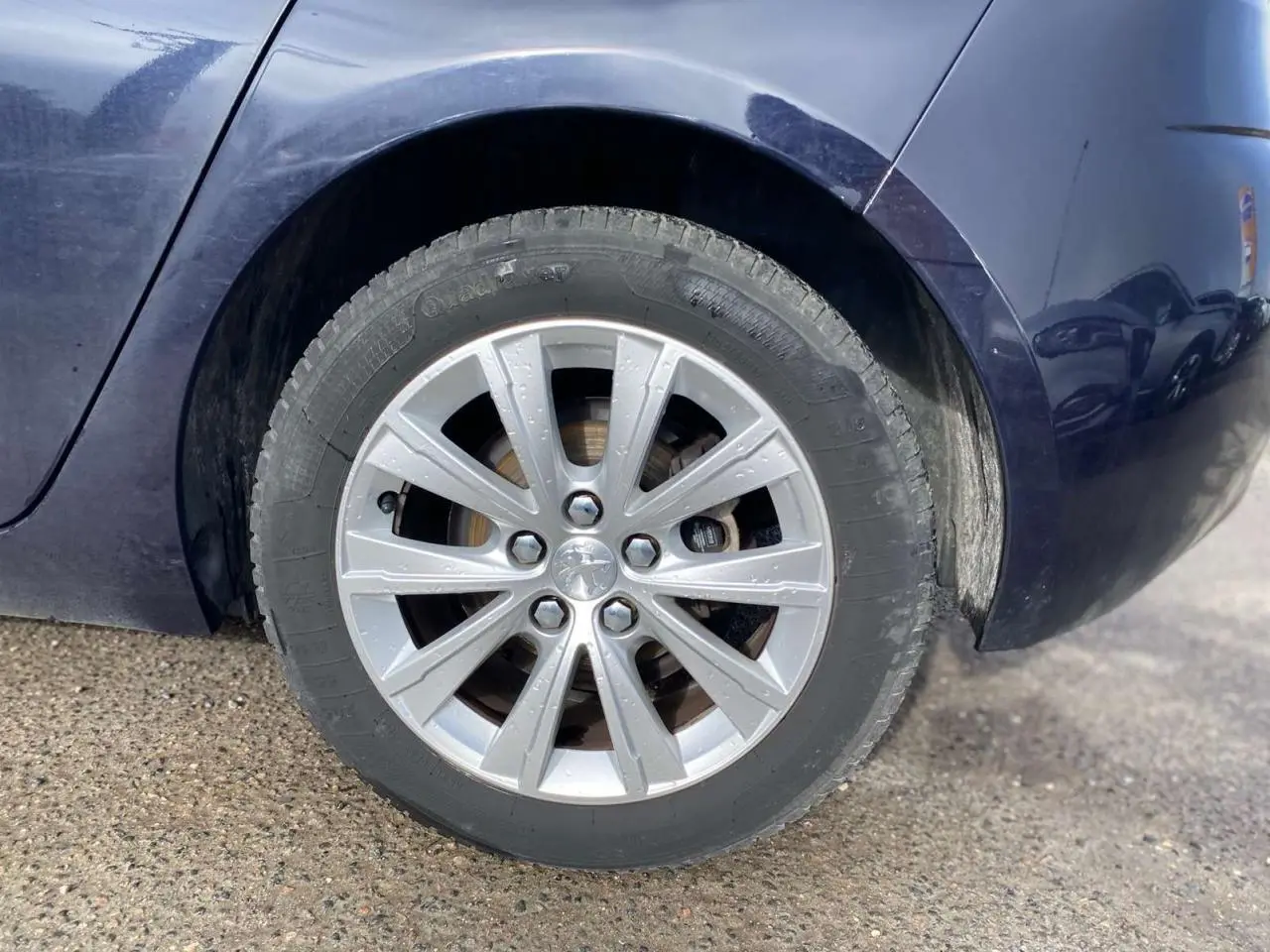 Gros plan sur la roue arrière droite d'une Peugeot 308 bleu foncé, avec jante alliage et carrosserie métallisée visible.