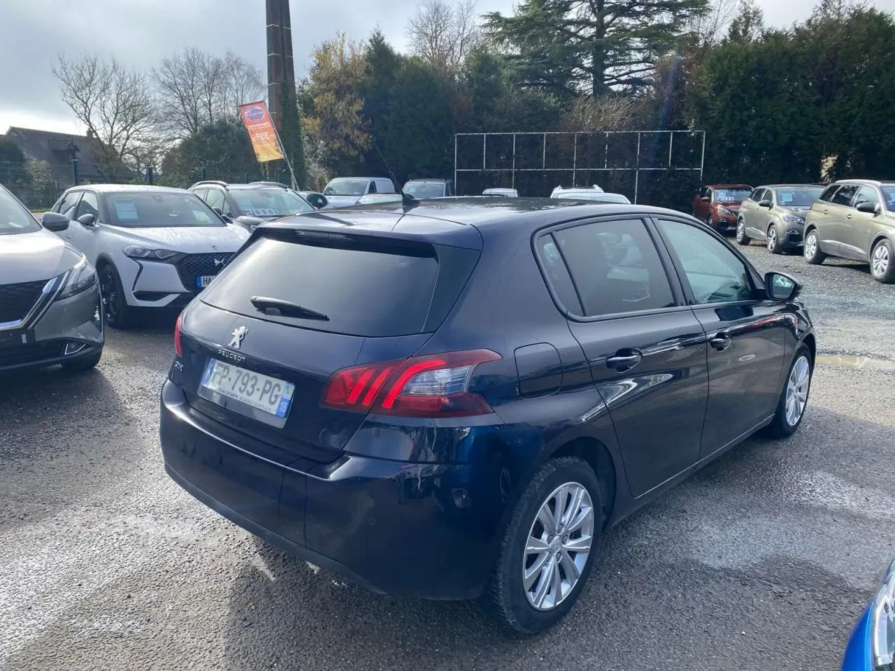 Peugeot 308 bleu foncé vue 3/4 arrière droit, avec feux arrière LED et jantes alliage visibles.