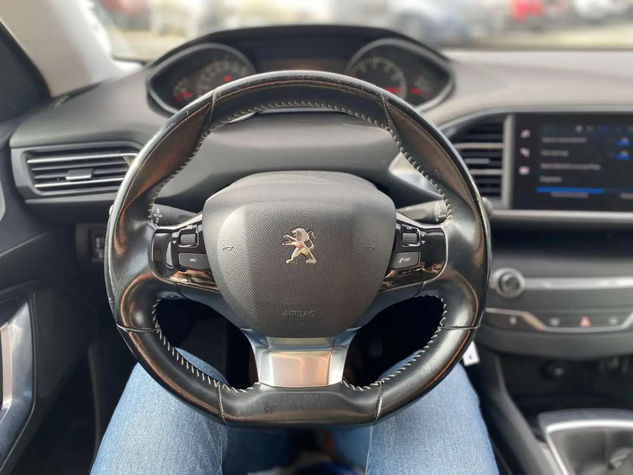 Vue intérieure centrée sur le volant cuir noir de la Peugeot 308 2018 avec tableau de bord et écran tactile visible.
