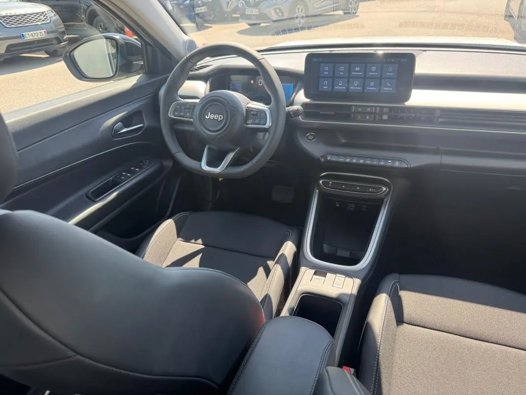 Intérieur du Jeep Avenger électrique 2025 vu côté conducteur, avec volant cuir, écran tactile et console centrale noire.