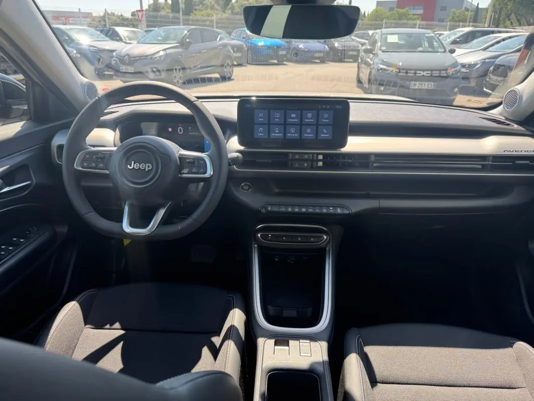 Vue intérieure avant du Jeep Avenger électrique 2025, tableau de bord moderne avec écran tactile central et volant cuir.