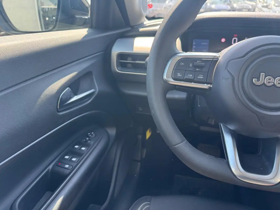 Vue intérieure côté conducteur du Jeep Avenger électrique blanc 2025, volant cuir et commandes au volant visibles.