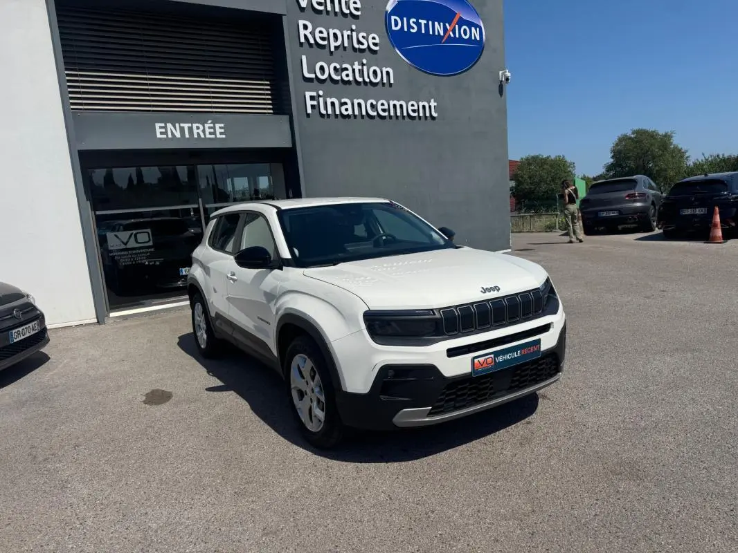 Jeep Avenger électrique blanc en 3/4 avant droit, avec jantes alliage 17 pouces, stationné devant un bâtiment commercial.