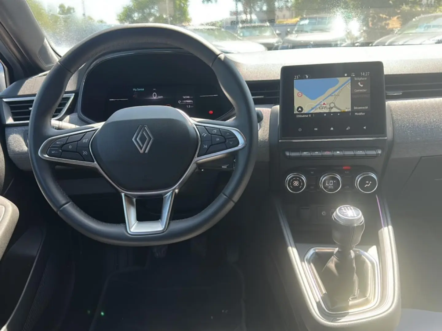 Vue frontale de l'intérieur de la Renault Clio V gris rafale, volant multifonction et écran tactile avec GPS visible.