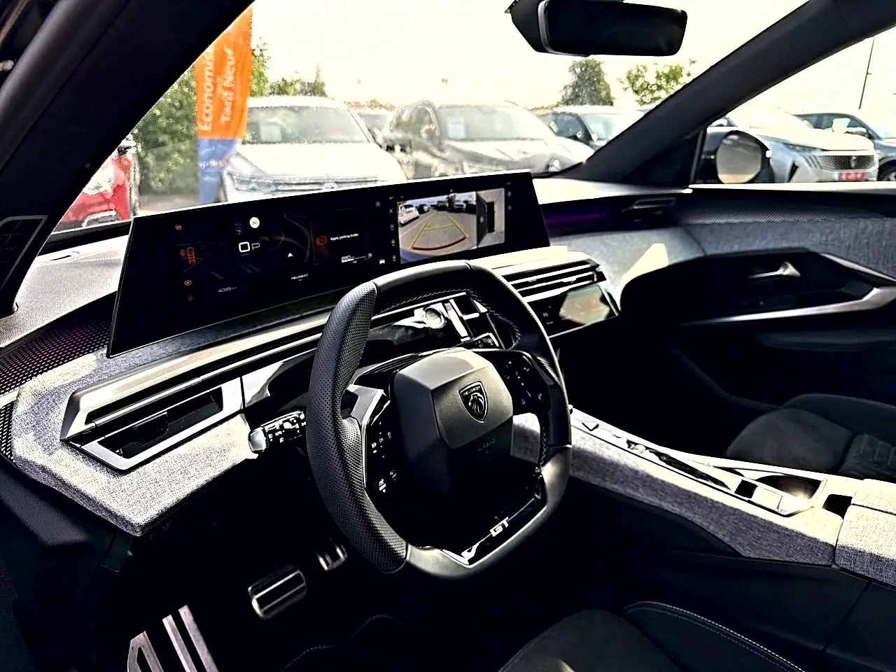 Vue intérieure côté conducteur du Peugeot 5008 Hybrid 145 GT e-dcs6 2025, tableau de bord moderne avec écran large et volant cuir noir.