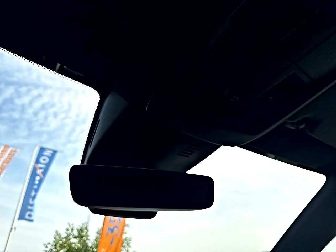Vue intérieure du pare-brise et du rétroviseur central d'un Peugeot 5008 noir, avec ciel et drapeaux en arrière-plan.