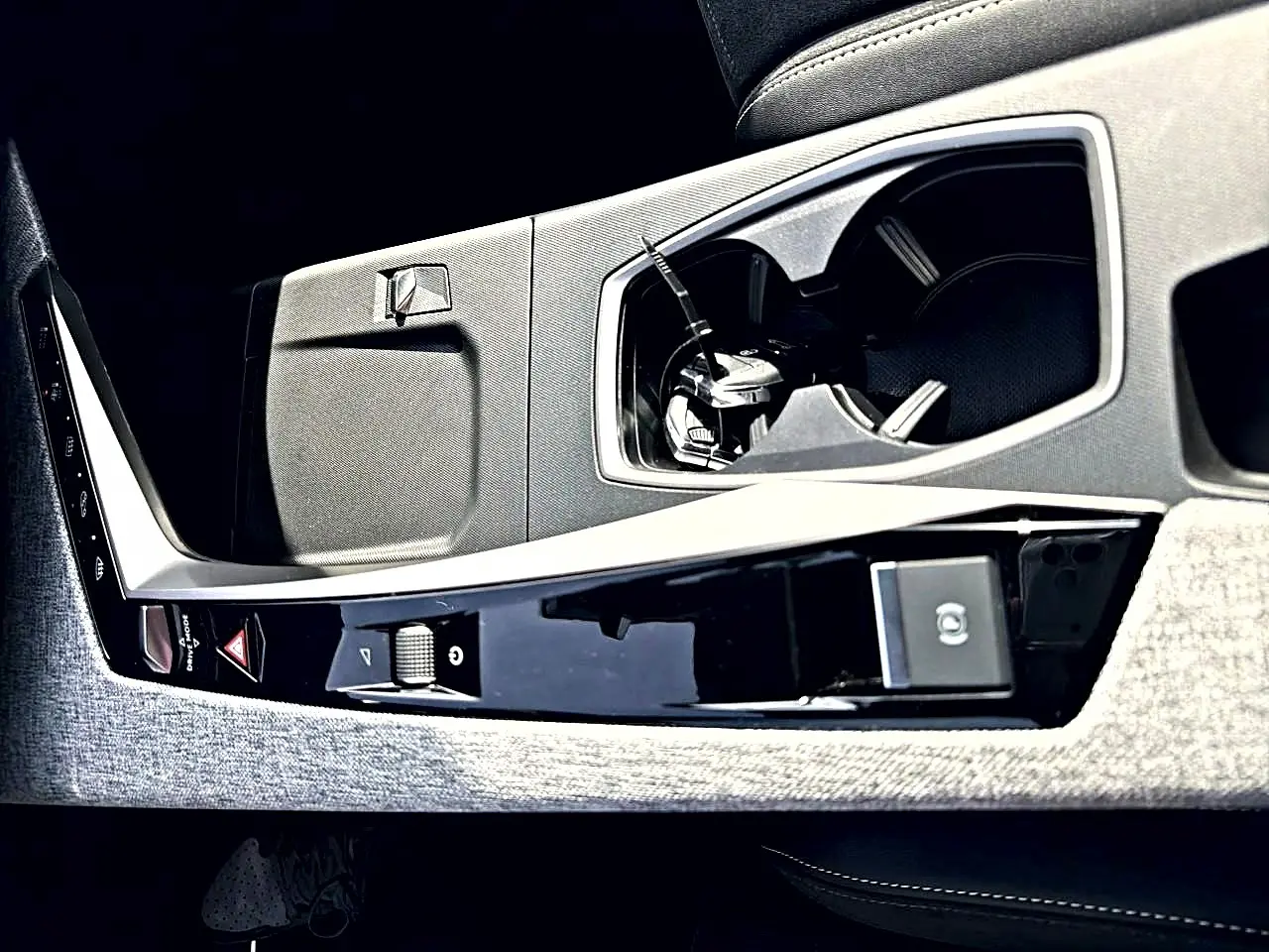 Détail de la console centrale intérieure du Peugeot 5008 Hybrid 145 GT e-dcs6 2025, avec porte-gobelets et commandes noires.