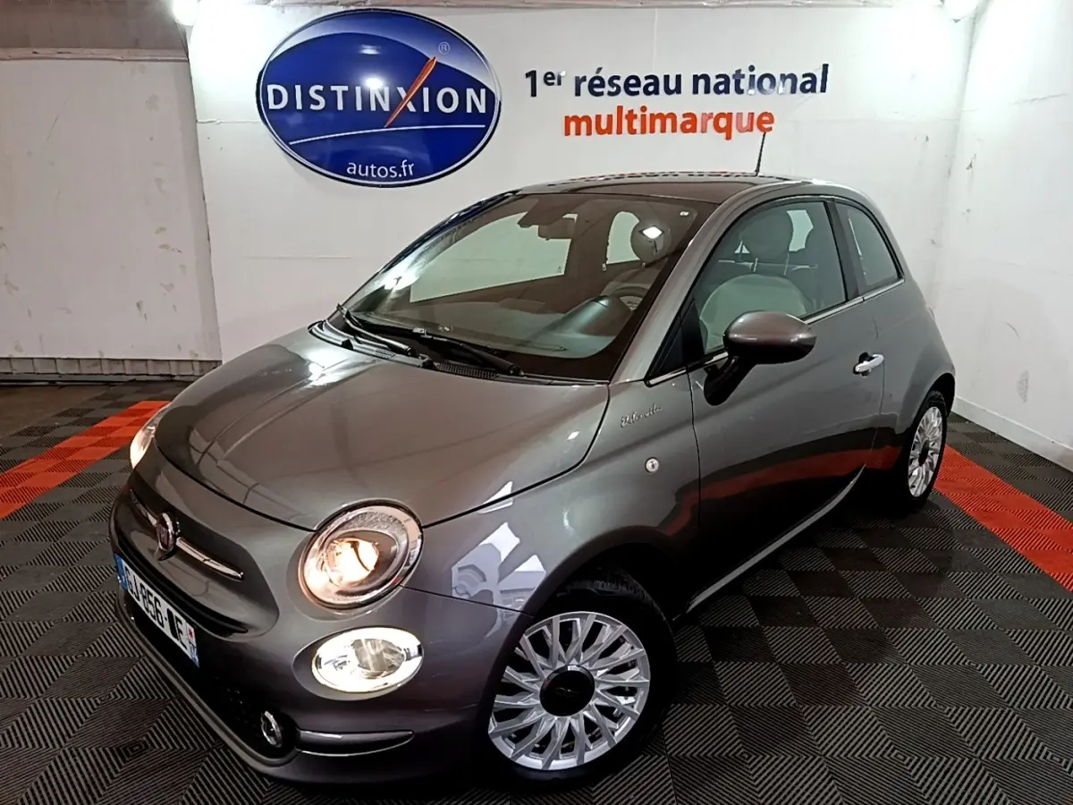 Vue 3/4 avant droite d'une FIAT 500 gris foncé avec phares allumés dans un showroom intérieur.