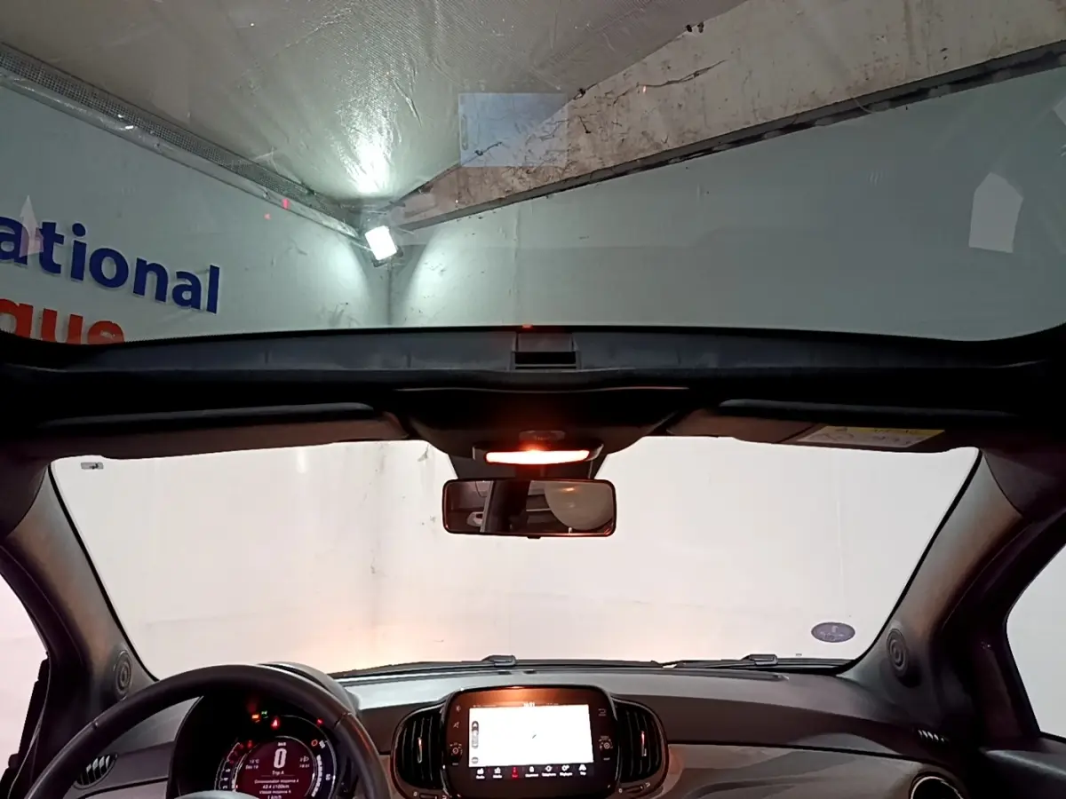 Vue intérieure avant de la Fiat 500 gris foncé 2022, avec tableau de bord numérique et toit panoramique ouvert.