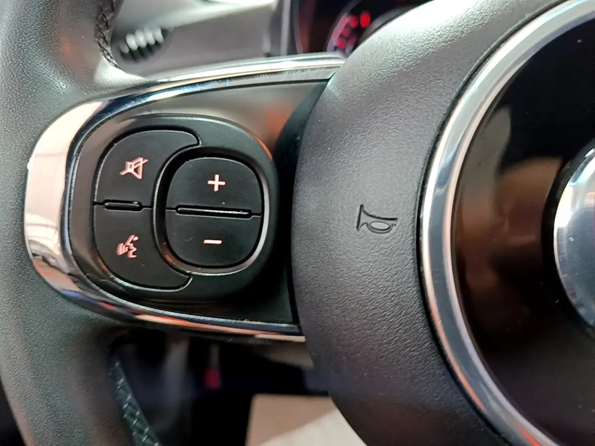 Gros plan sur les commandes gauche du volant cuir du Fiat 500 gris foncé, avec boutons de volume et commande vocale.