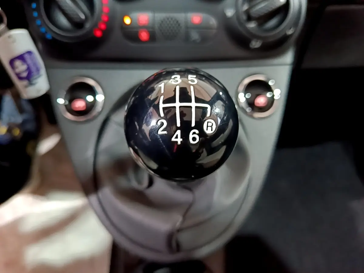 Gros plan sur le levier de vitesses manuel noir de la FIAT 500 gris foncé, avec tableau de bord en arrière-plan flou.