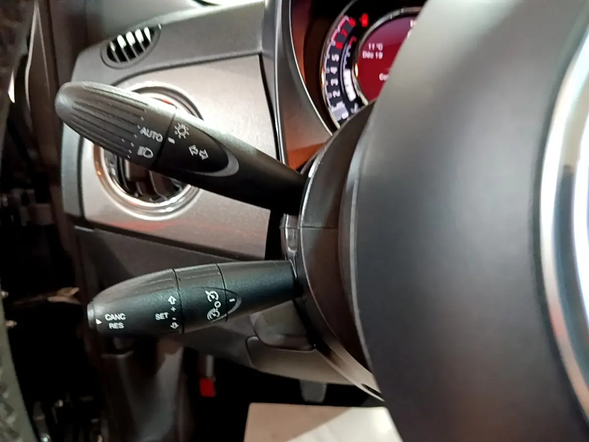 Gros plan sur les commandes au volant d'une FIAT 500 gris foncé, montrant les leviers de clignotants et régulateur.