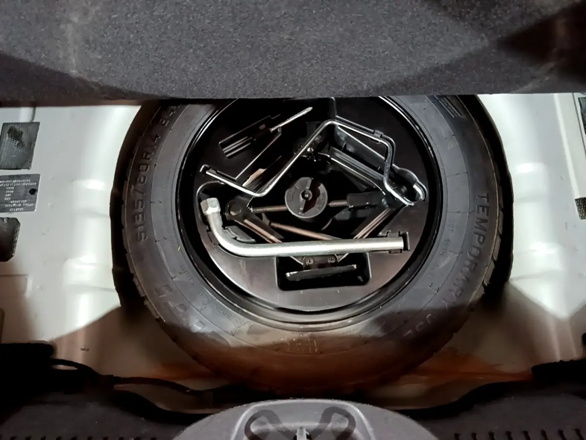 Gros plan sur la roue de secours et les outils de bord dans le coffre d'une Fiat 500 gris foncé, vue de dessus.